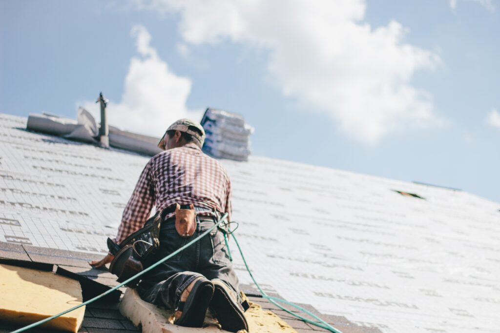 Roofer laying shingles on roof with safety harness.