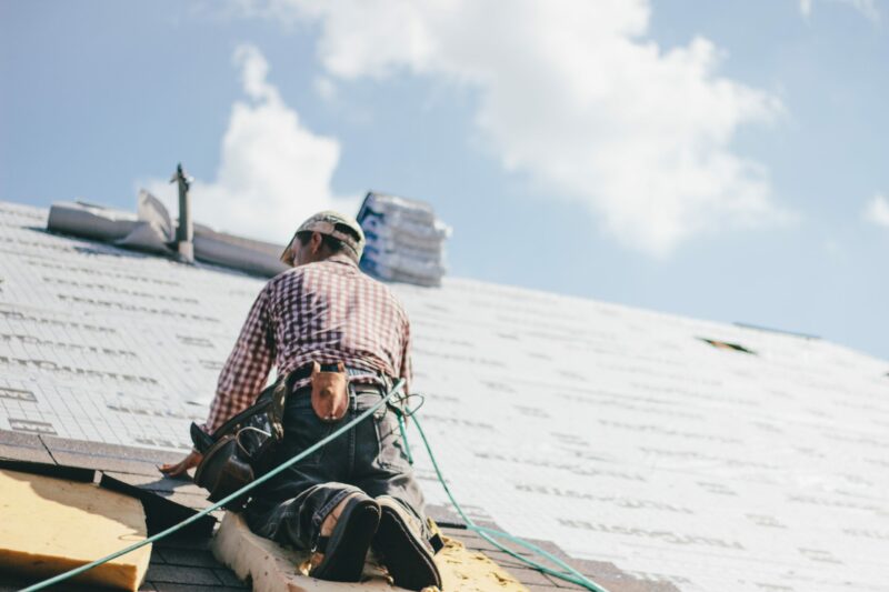 Roofer laying shingles on roof with safety harness.