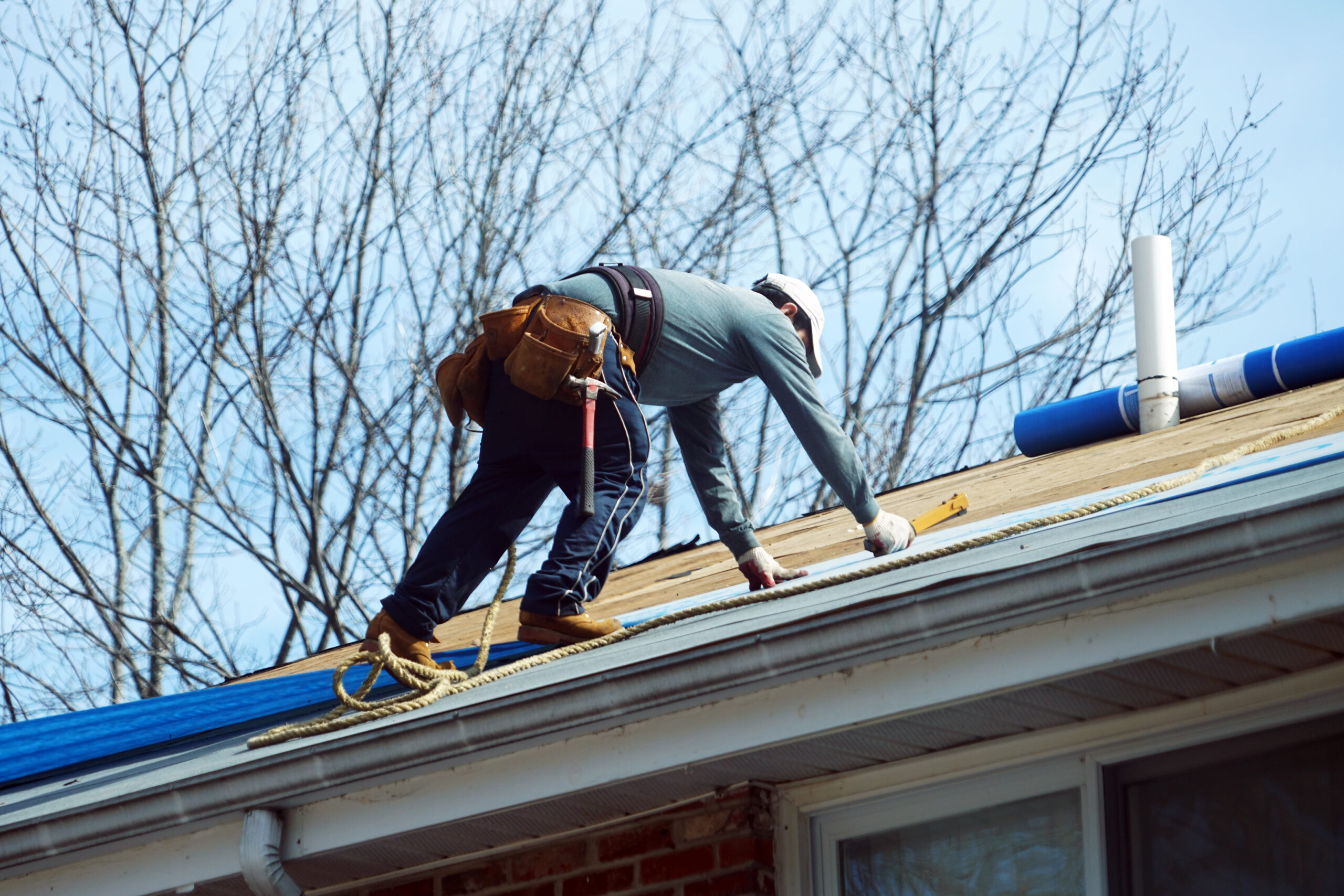 Roofer climbing roof with tool belt and safety harness on